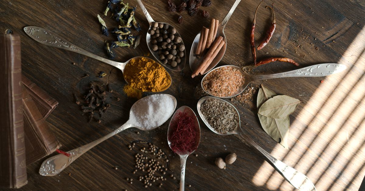 A top view of various spices arranged on a wooden surface with spoons, showcasing culinary richness.